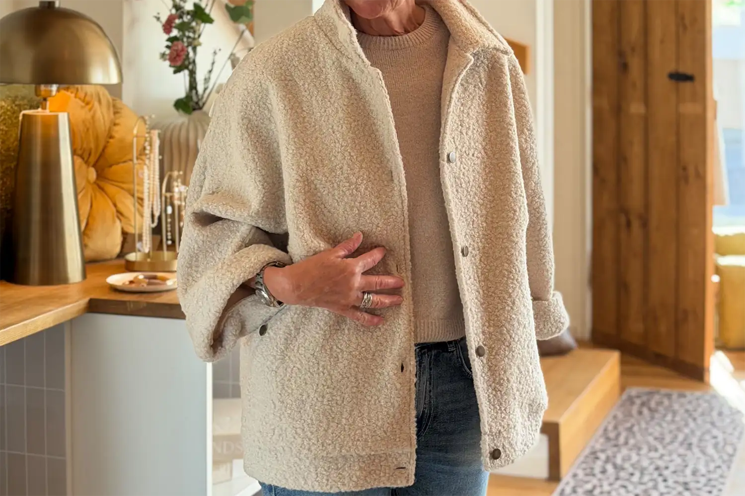 monas_store-gutennberg-herbst-jacke-teddy Person trägt eine cremefarbene Bouclé-Jacke über einem beigen Strickpullover und Jeans.
